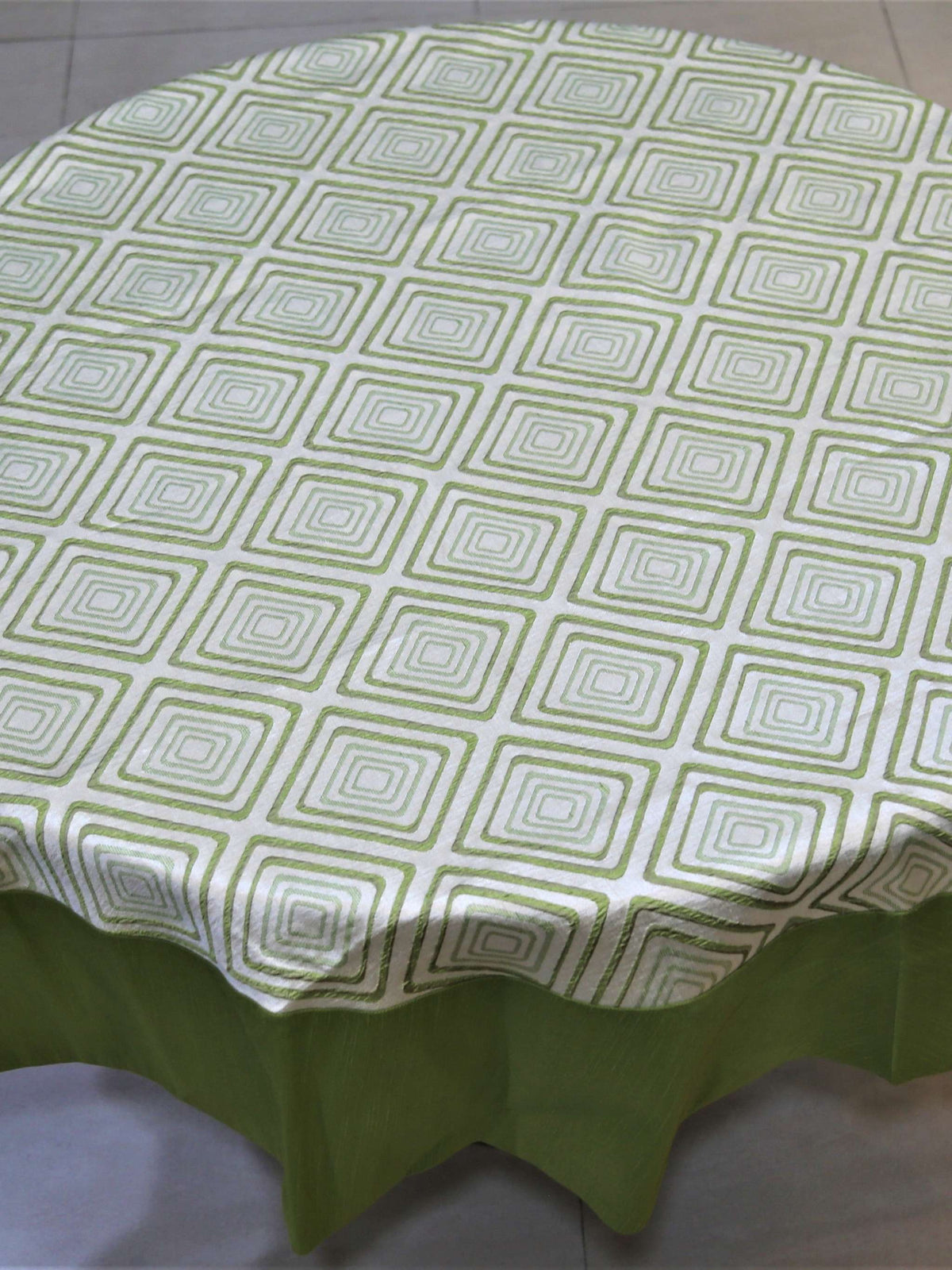 Round table cover with a cream geometric diamond print on top and a solid olive-green underskirt