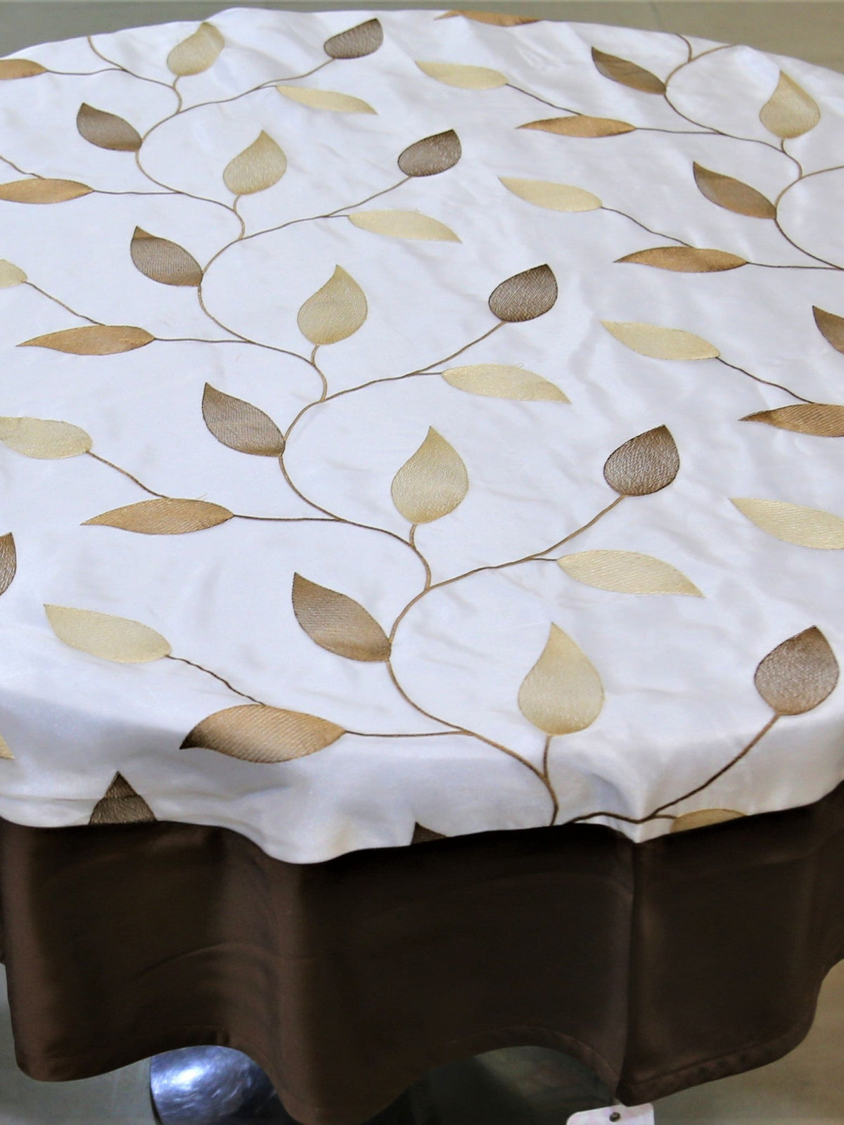 Round cream table cover with a beige-gold embroidered leaf-vine pattern and a solid dark brown underskirt