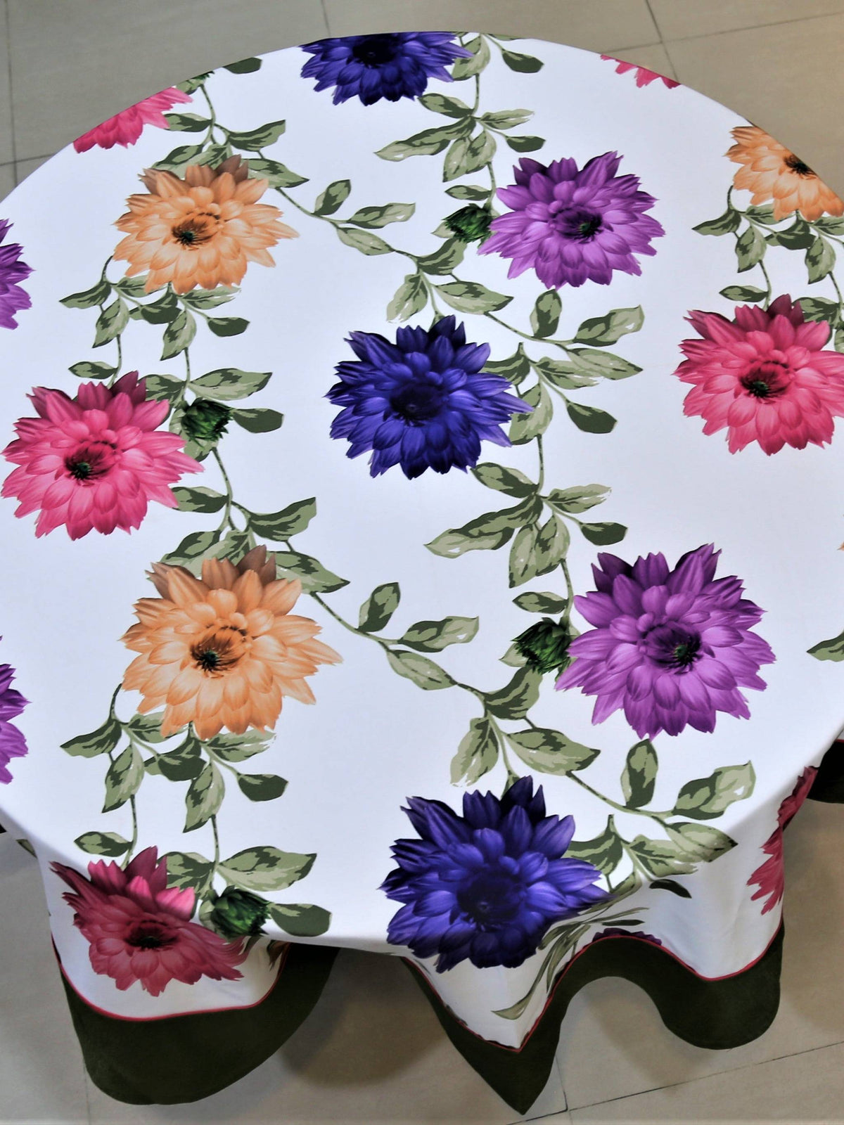 Round white table cover with a large multicolour floral print and a solid olive-green underskirt with red piping