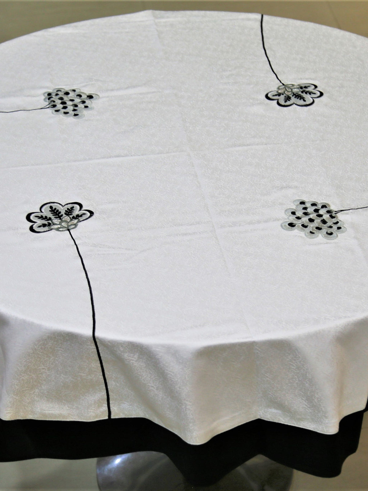 Round cream table cover with scattered black-outlined floral appliqué medallions and a black underskirt