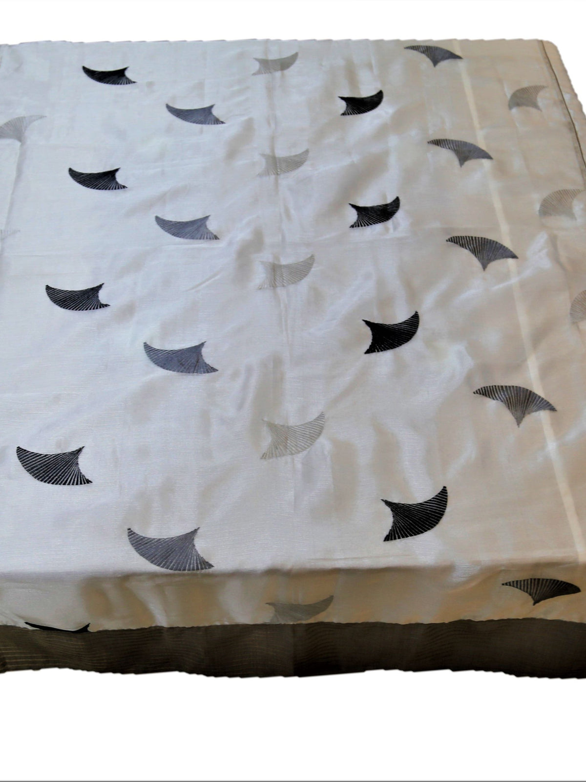 White table cover with grey embroidered fan-shaped motifs and a beige striped border
