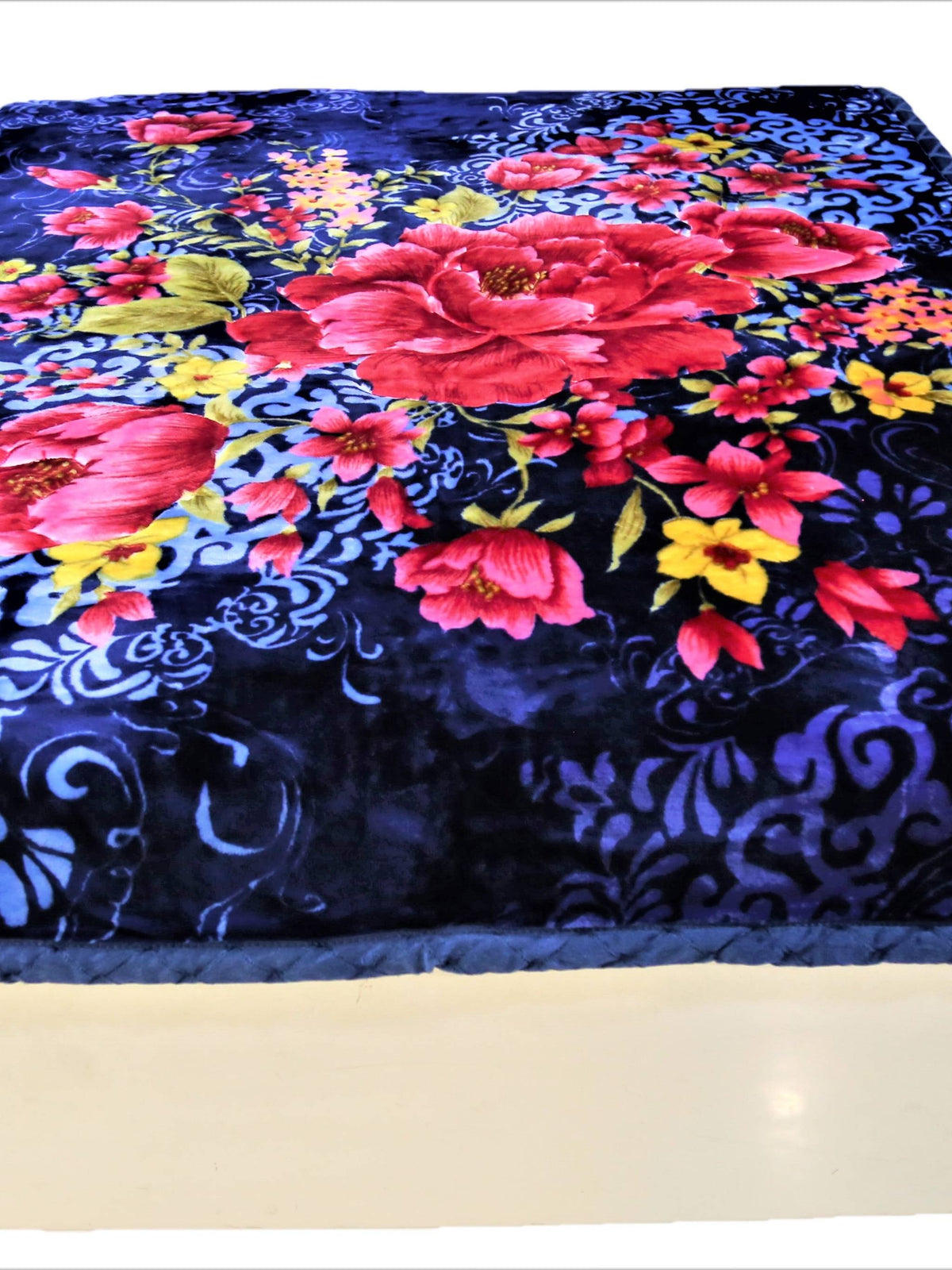 Navy-blue velour blanket with a large red-pink peony floral print and pale-blue scroll damask pattern, folded at the foot of a bed