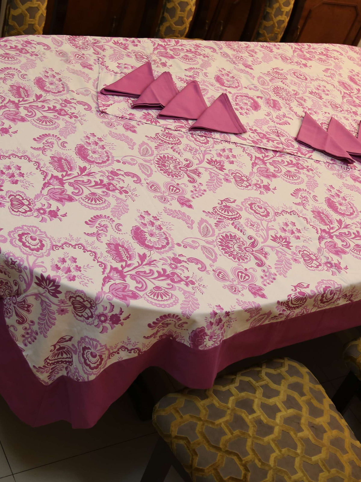 Off-white oval table cover set with a pink and purple paisley floral print, a solid mauve-pink border, and matching mauve triangle-folded napkins