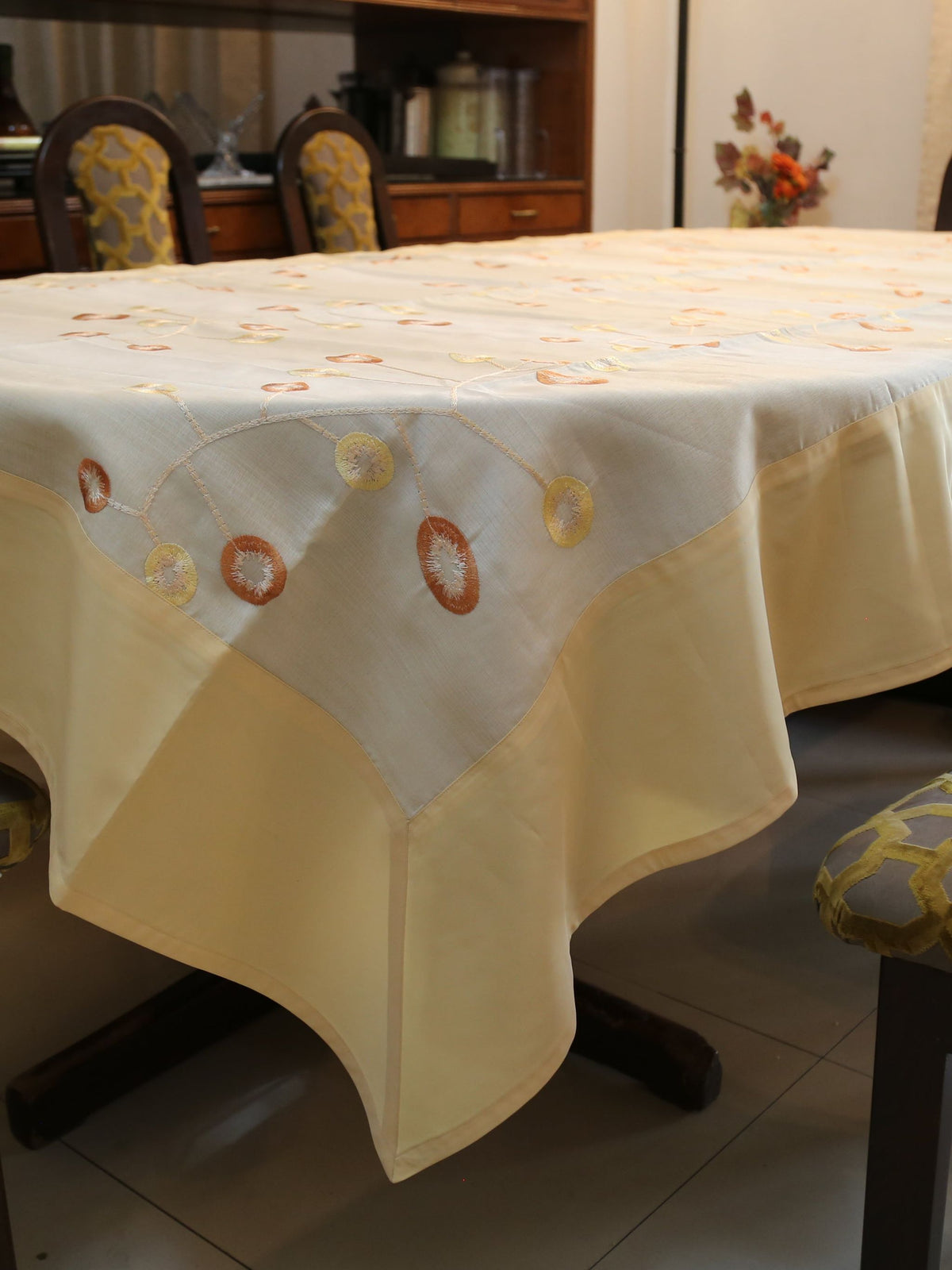Cream oval table cover with a rust-orange and gold ring embroidery vine pattern and a solid cream border