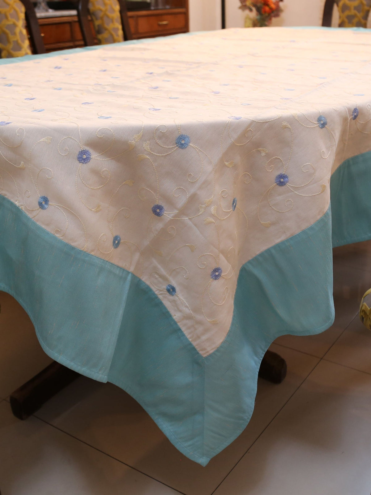 White oval table cover with small blue embroidered flower-and-vine dots and a solid aqua-teal border