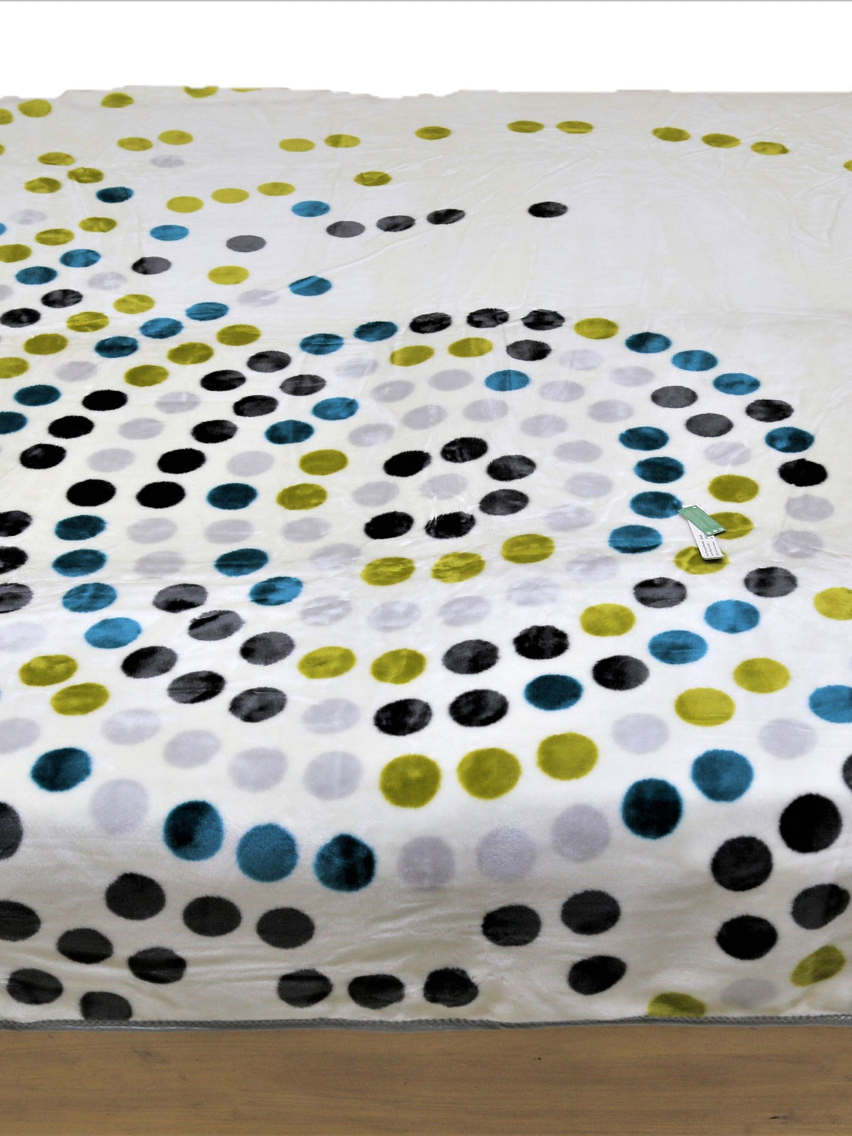 White-cream blanket with a swirled spiral polka-dot pattern in black, teal-blue, olive-green, and light-grey circles, folded on a bed