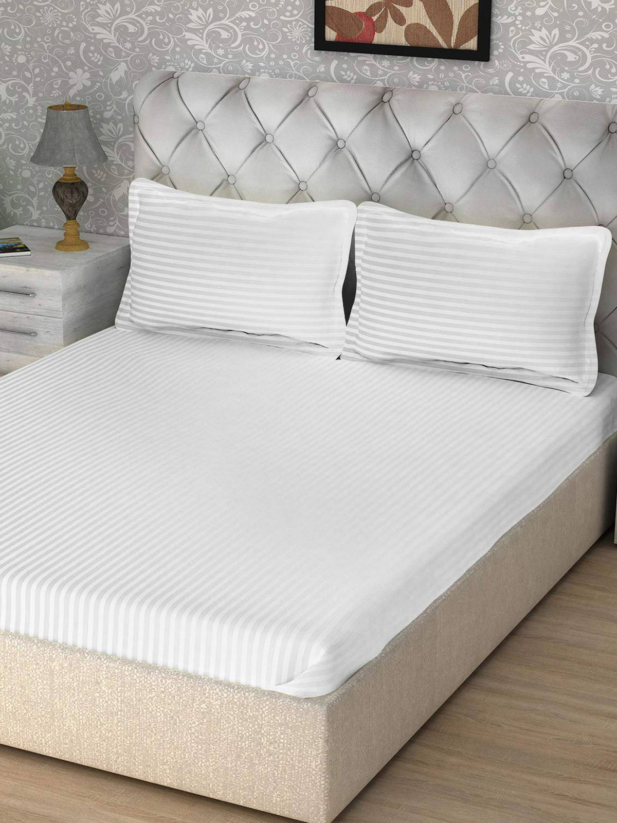 Solid white satin-stripe cotton bedsheet with matching pillow covers on a tufted grey velvet headboard bed