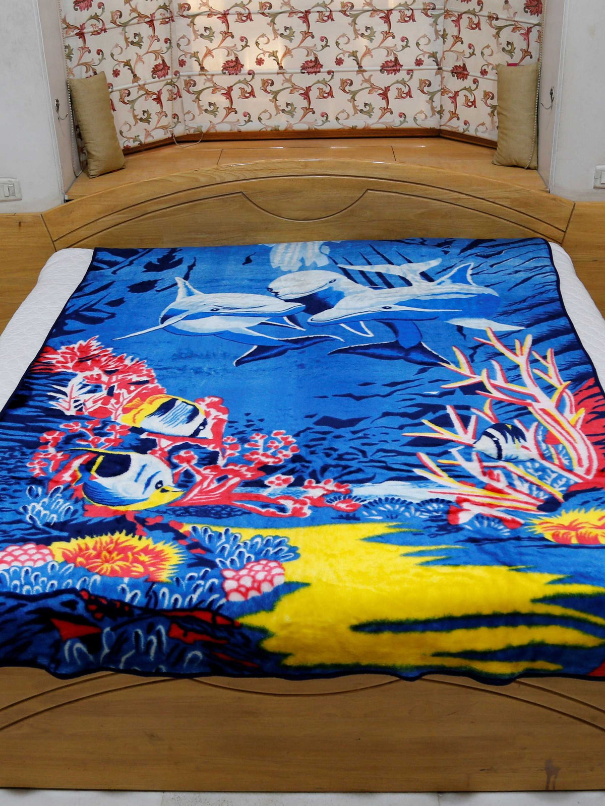 Royal-blue blanket with a printed underwater scene of dolphins, coral reef, and tropical fish, spread flat over a bed