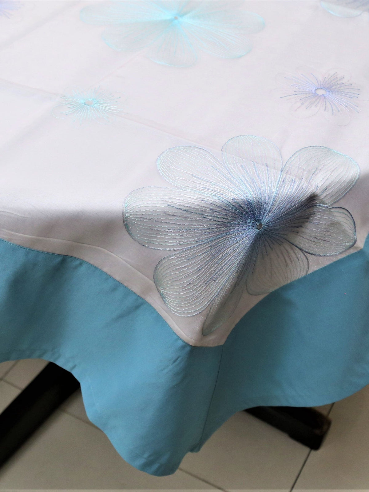 White oval table cover with a blue and purple embroidered flower pattern and a solid teal-blue border