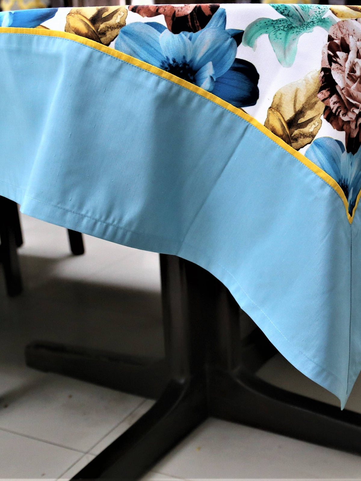 White table cover with a large blue, brown, and teal floral print and a solid light-blue underskirt with gold piping