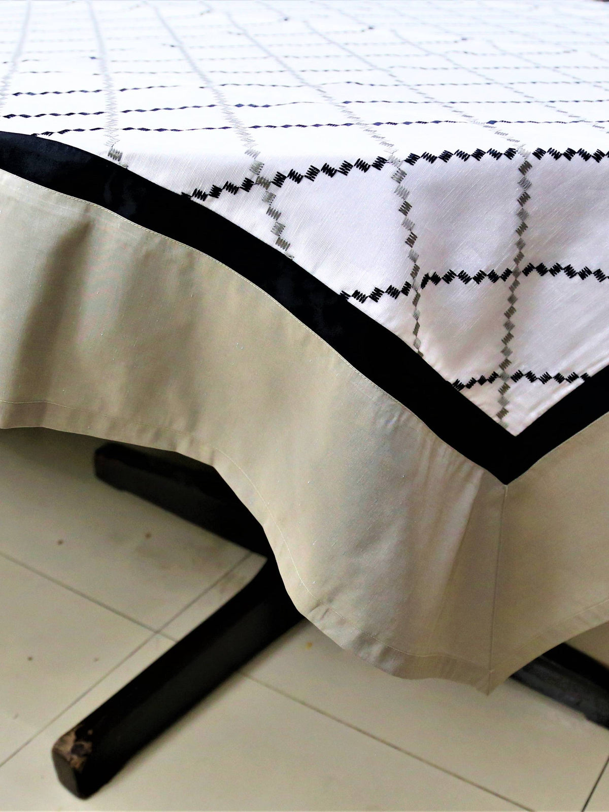 White table cover with a black and grey diamond-lattice embroidered pattern and a plain beige-tan underskirt with a black edge trim