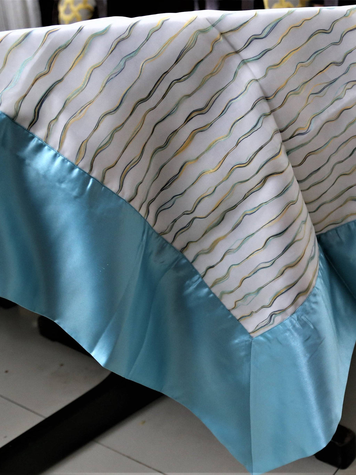 Cream table cover with a wavy multicolour stitch-line pattern and a solid sky-blue satin border