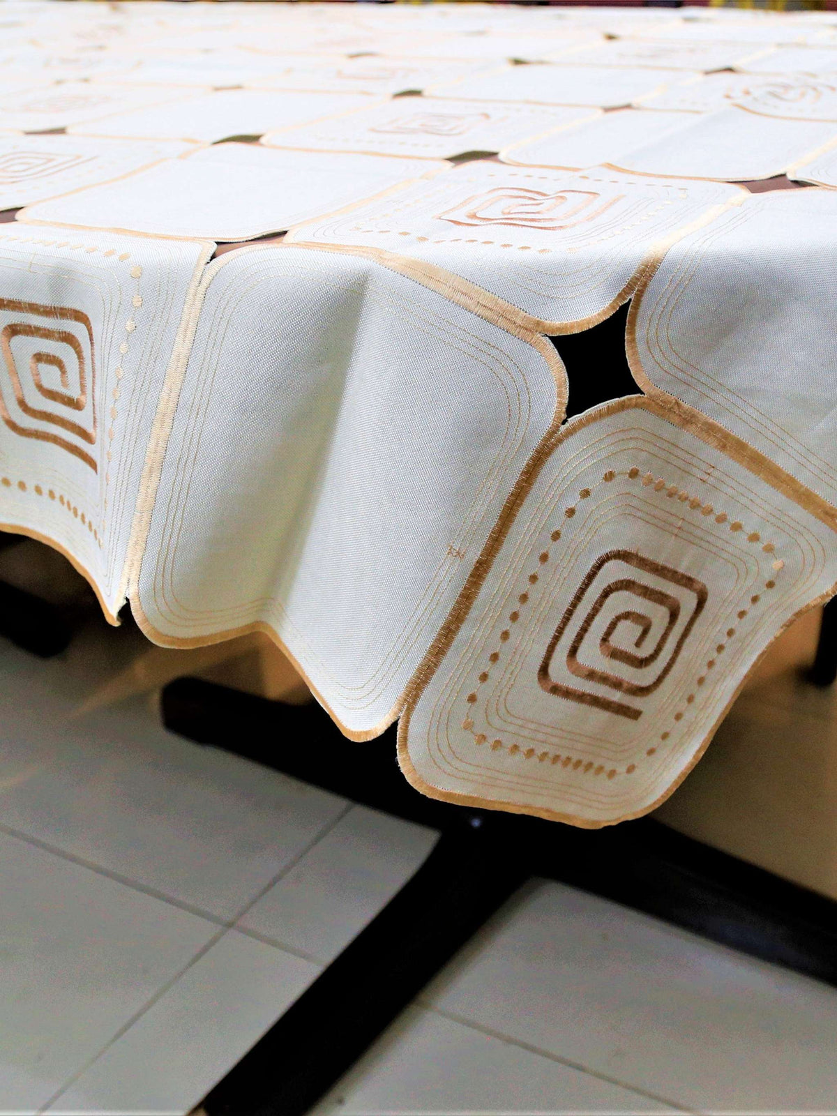 White-ivory table cover with a geometric cutwork square pattern and brown scroll motifs inside each square