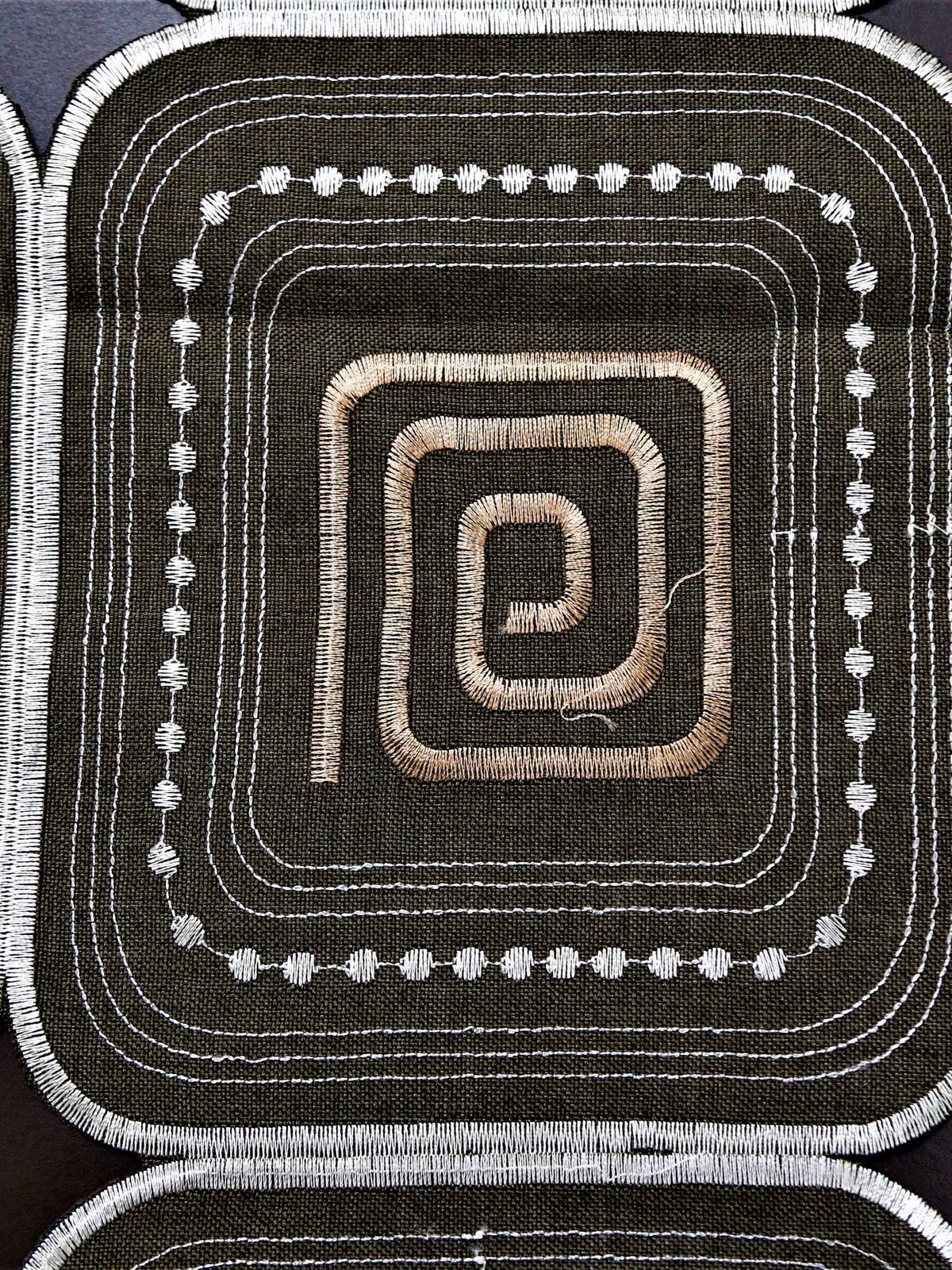 Brown table cover with a cutwork square pattern and copper spiral motifs inside each square