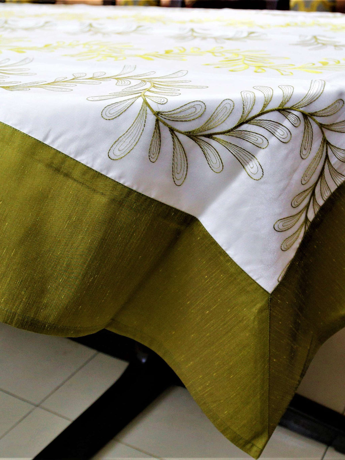 White table cover with a green and yellow embroidered fern-leaf vine pattern and a solid olive-green underskirt