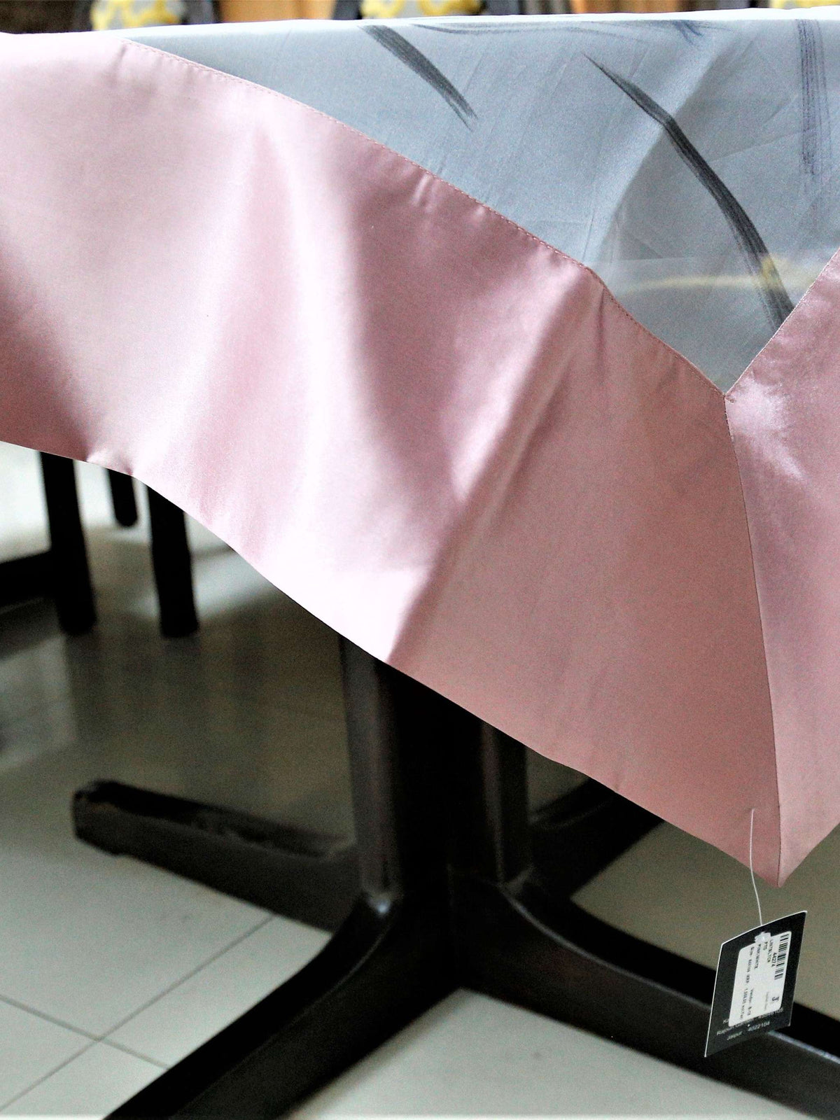 White table cover with a criss-crossing blue, pink, and grey stitch-line pattern and a solid blush-pink satin border