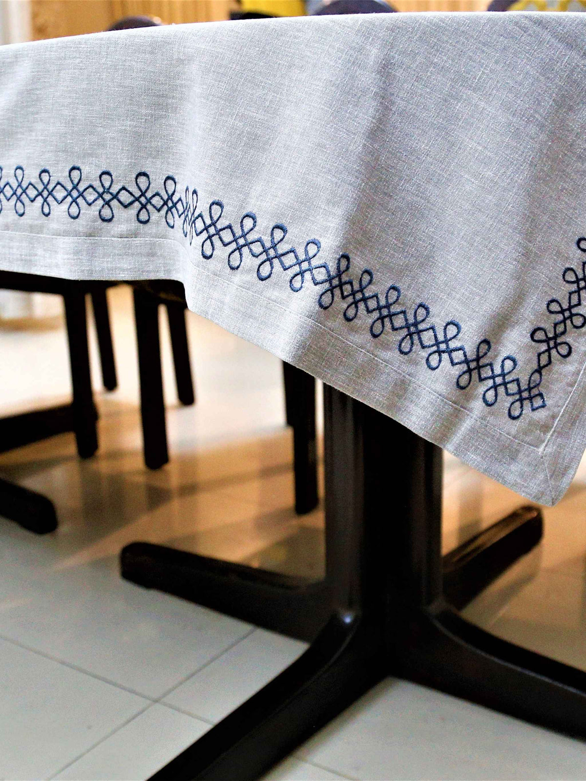 Light grey linen table cover with a navy embroidered scallop-chain border pattern