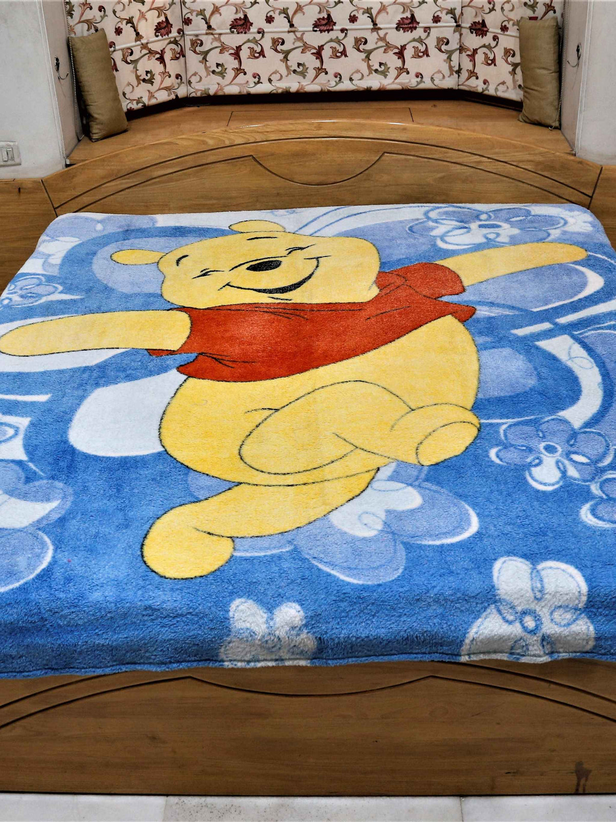 Blue plush blanket with a printed Winnie the Pooh design and white flowers, spread flat over a bed