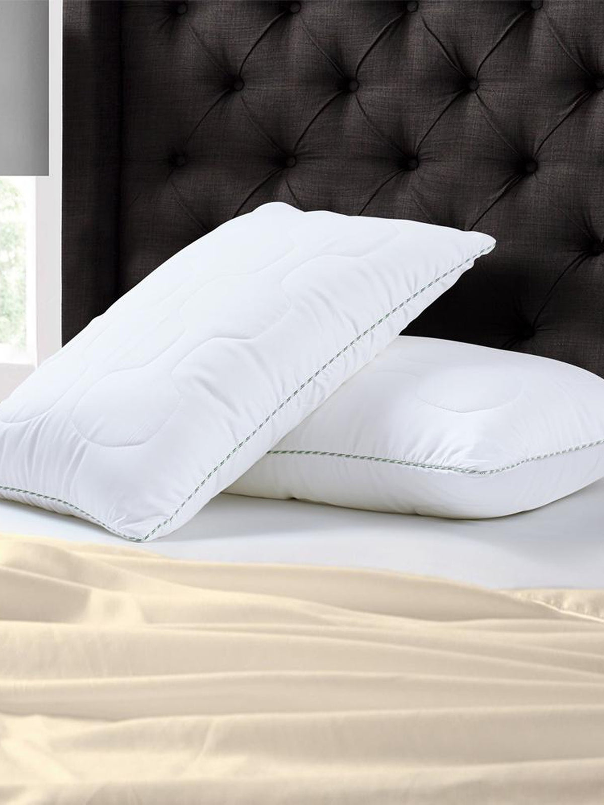 Two white quilted Tencel pillows against a dark tufted headboard, grey corded edge