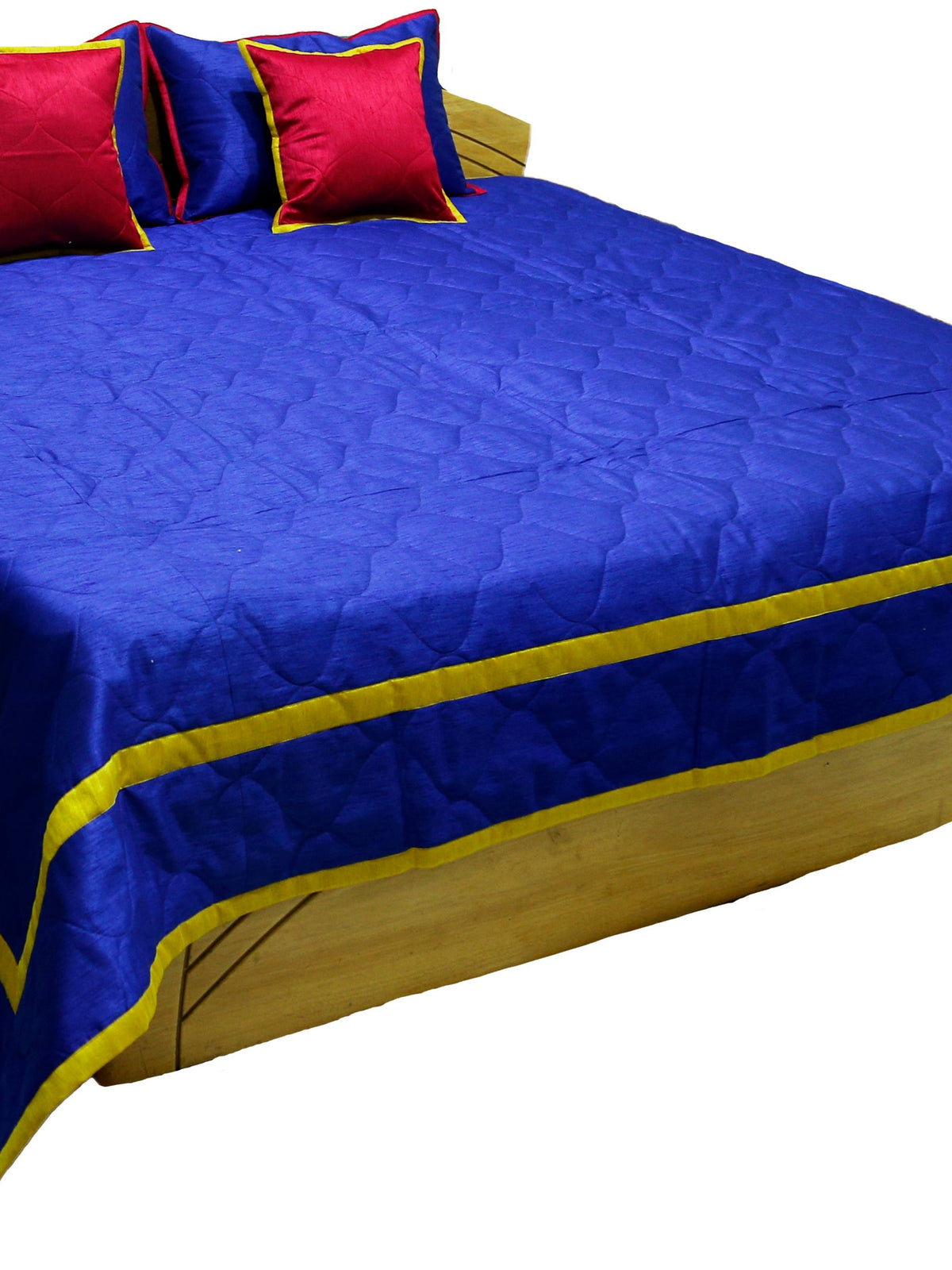 Royal blue quilted bedcover with gold piped border and crimson cushions, angled view