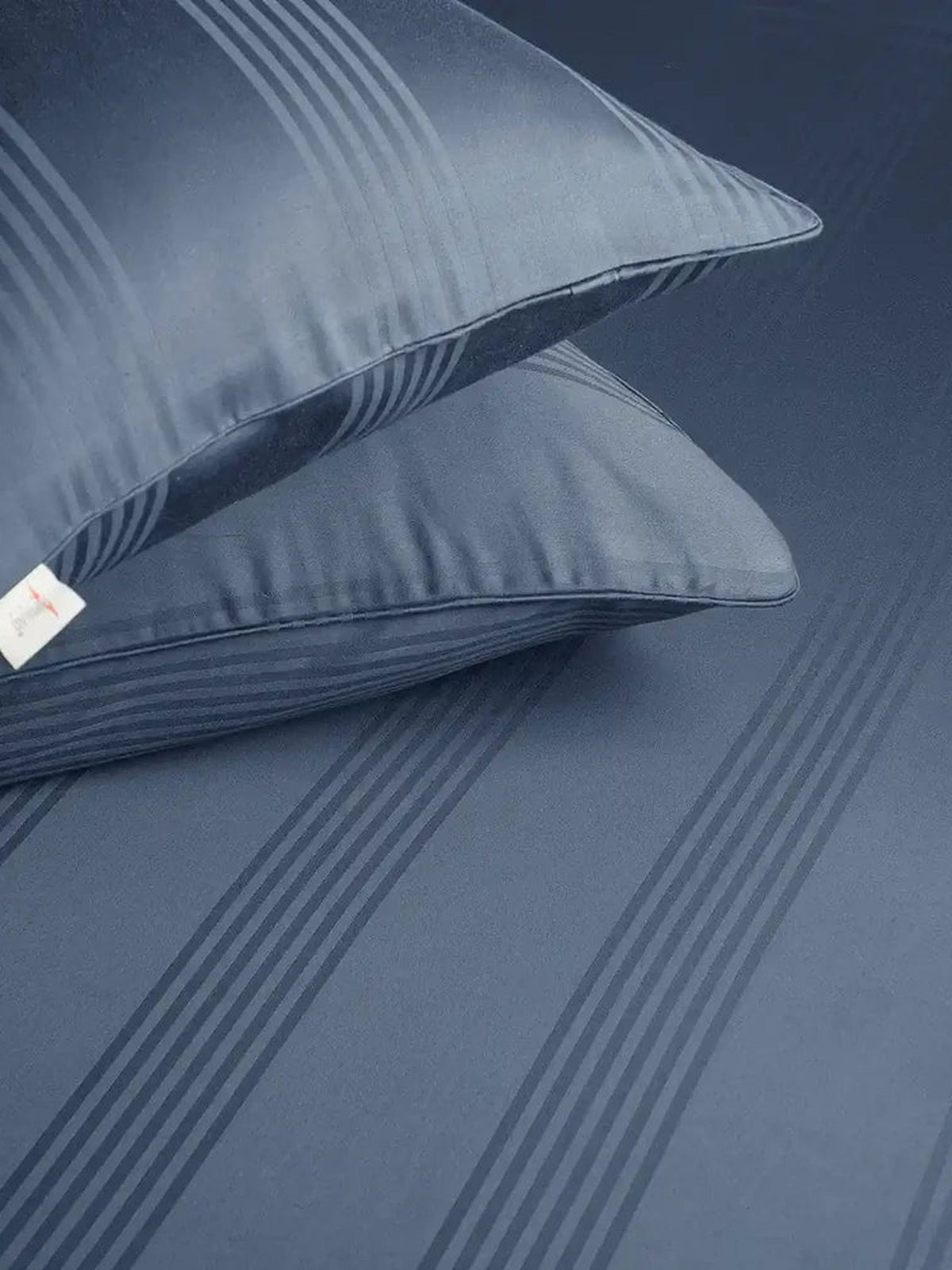 Two denim blue satin stripe pillow covers on the matching bedsheet, close-up
