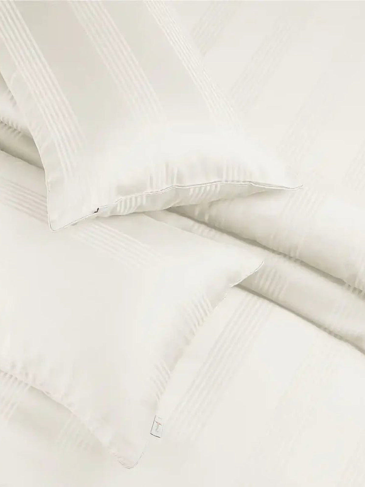 Two ivory satin stripe pillow covers on the matching bedding, close-up