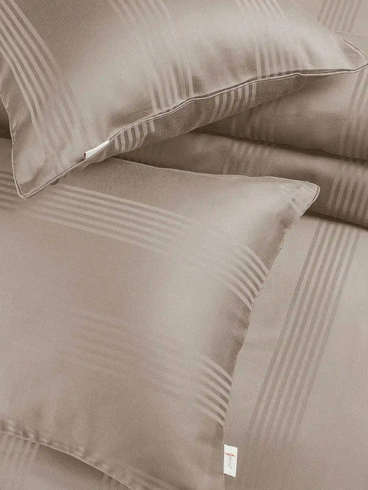 Two taupe satin stripe pillow covers on the matching bedding, close-up