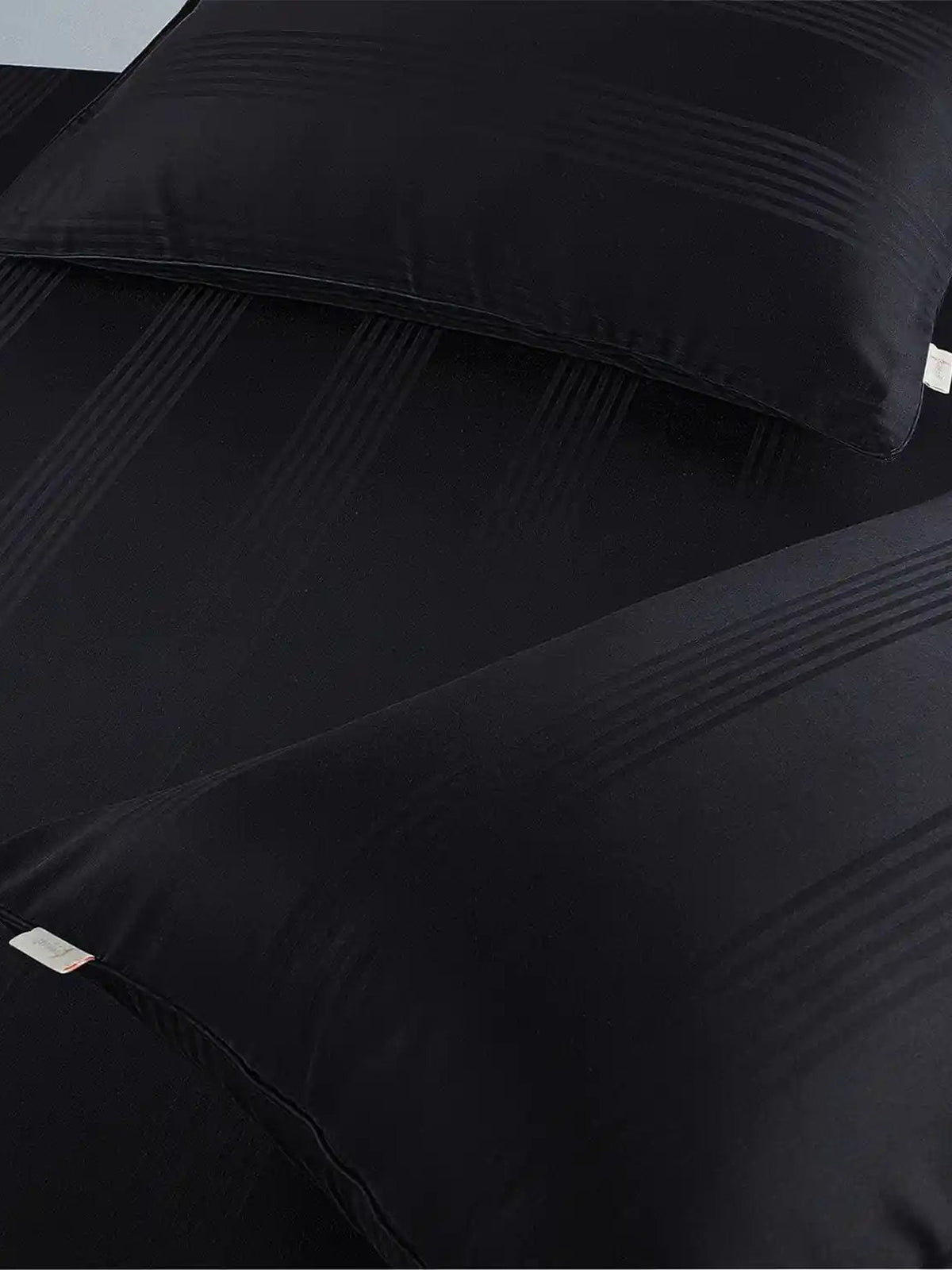 Two black satin stripe pillow covers on the matching bedding, close-up