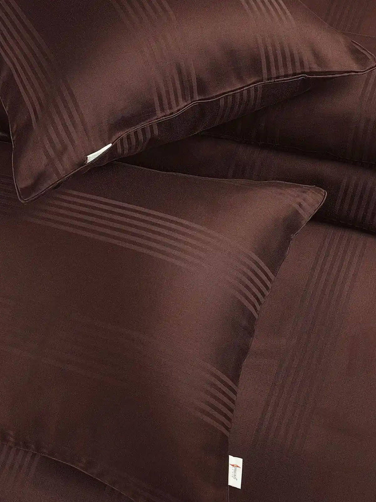 Two cocoa brown satin stripe pillow covers on the matching bedding, close-up