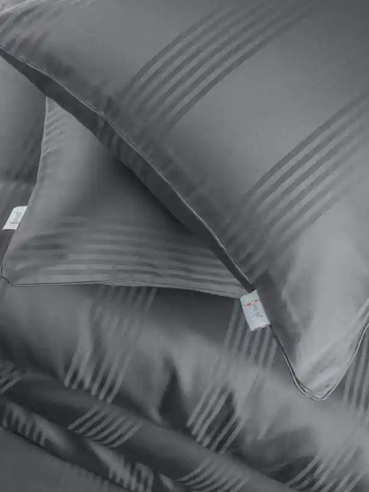 Two charcoal grey satin stripe pillow covers on the matching bedding, close-up