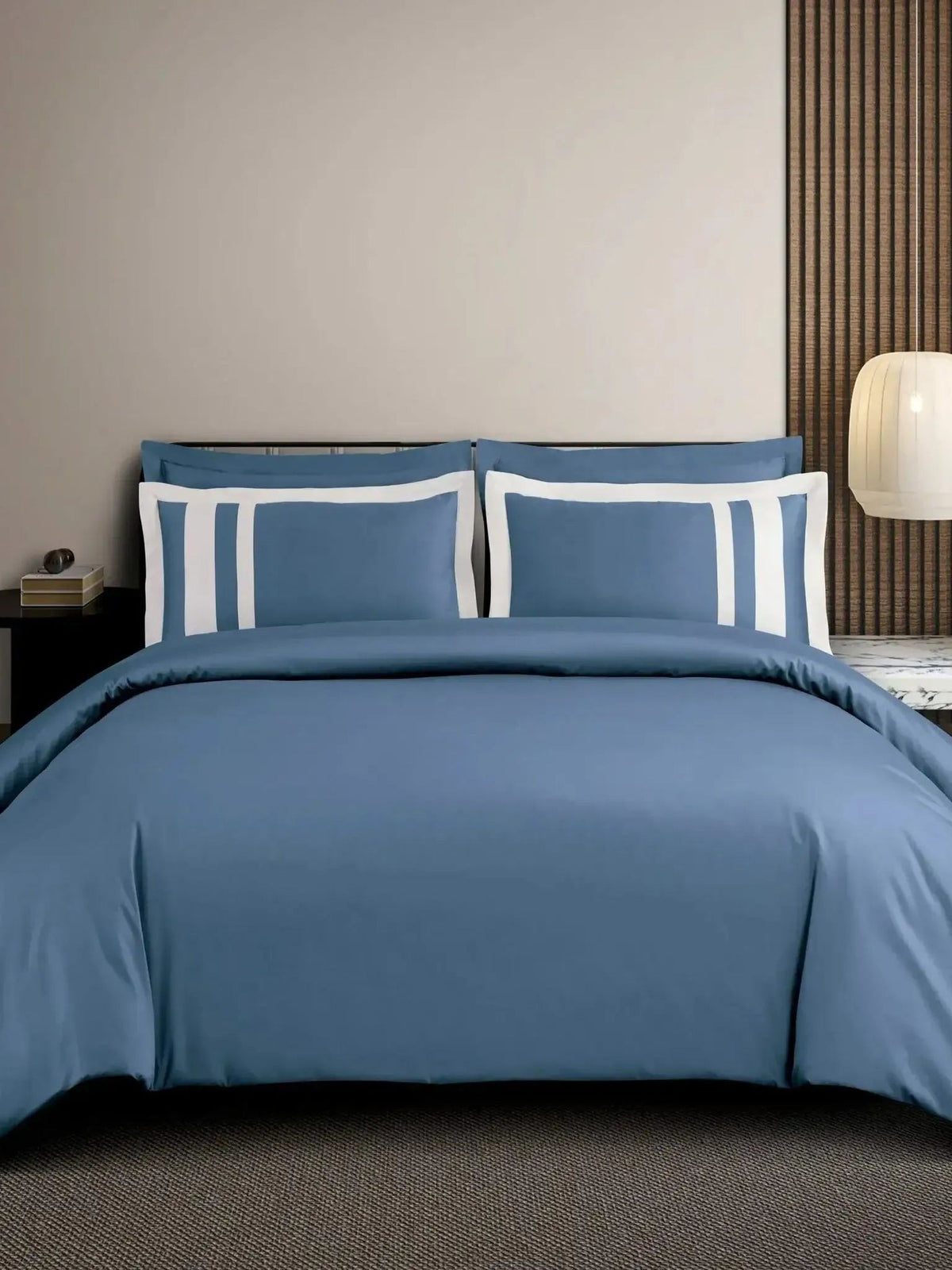 Slate-blue cotton bedsheet set with a white block-stripe border on the pillow covers, styled on a bed