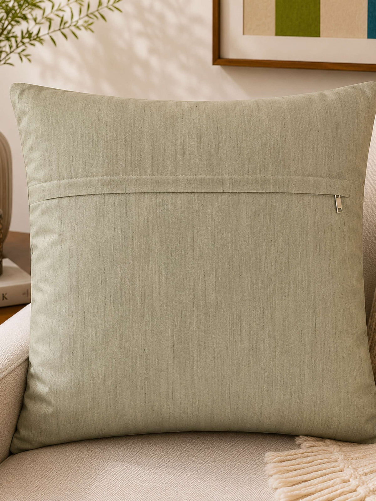 Same pale sage-green cushion cover, reverse side with concealed zip, staged on a sofa