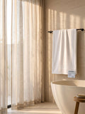White cotton bath towel with woven border hanging on a bathroom towel bar