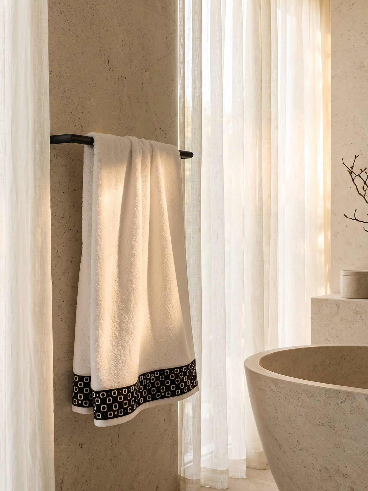 White cotton bath towel with black contrast woven border folded on a wooden bathroom shelf