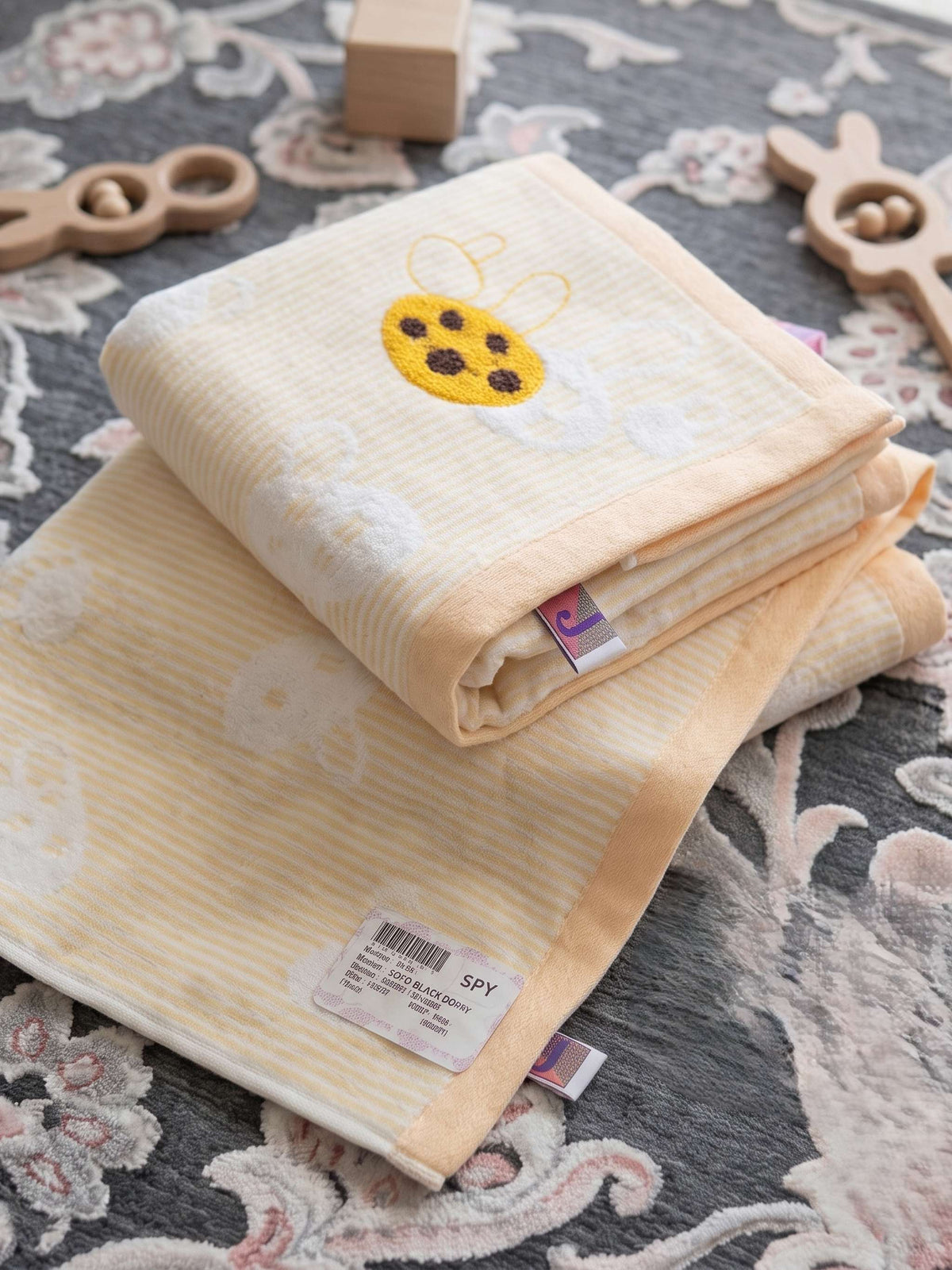 Yellow printed cotton bath towel with bee design folded on a wooden bathroom