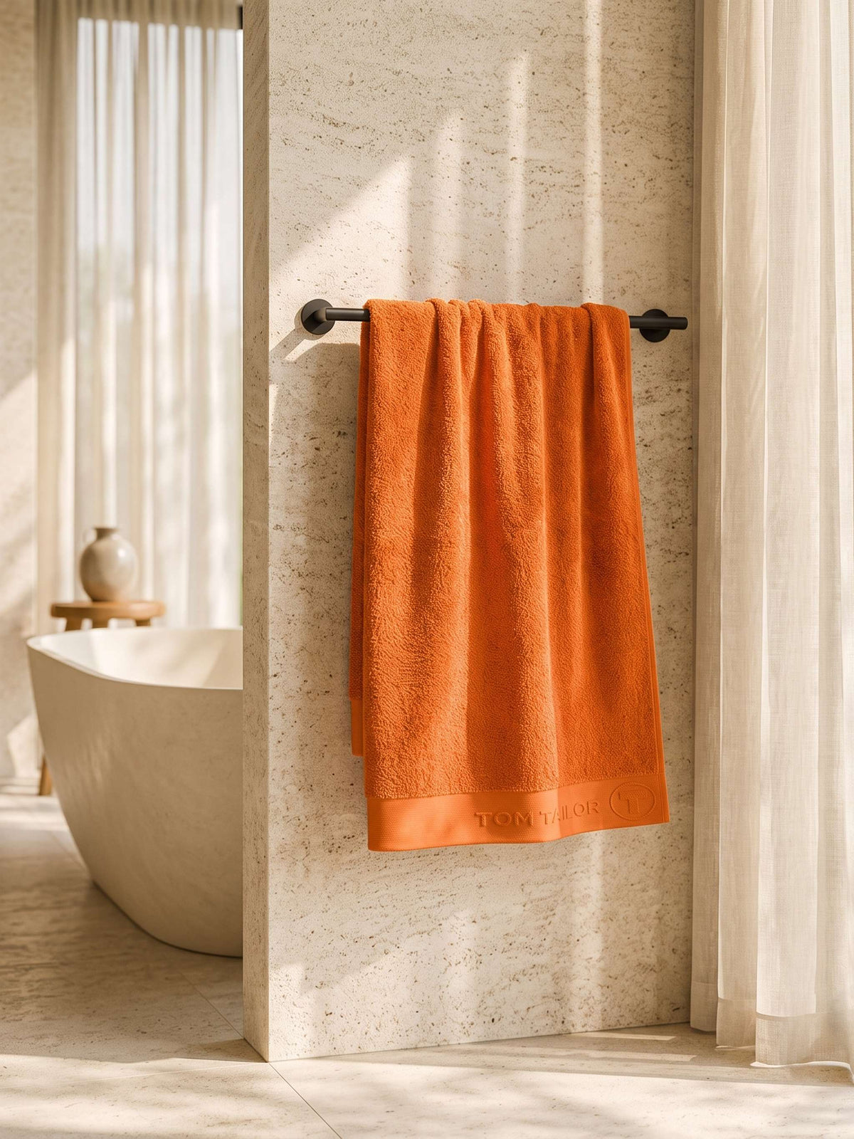 Orange cotton bath towel with woven border hanging on a towel rail in a modern bathroom 