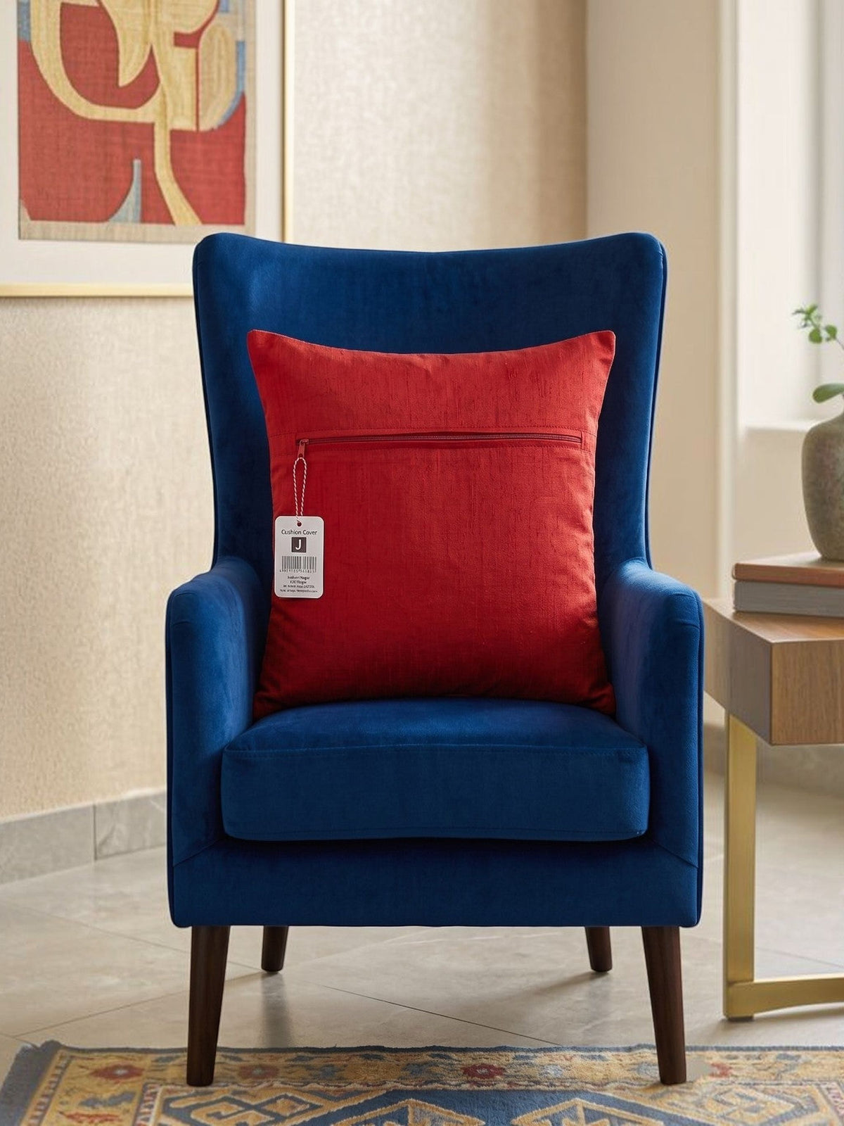 Red embroidered polysilk cushion cover with golden ornamental border design on a blue accent chair