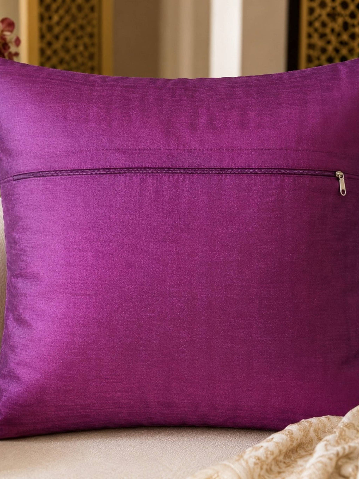 Purple pillow with a zipper on a beige couch with decorative elements.