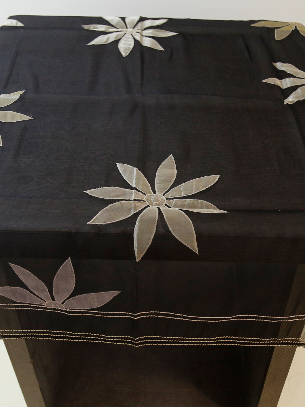 Black sheer organza table cover with a scattered cream appliqué flower pattern and a woven-stripe sheer border, draped over a small display table