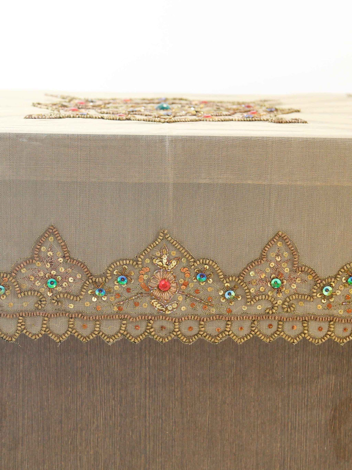 Beige net table cover with a hexagonal gold-beaded floral medallion embroidered at the centre, accented with red and turquoise stones, and a matching beaded scalloped border