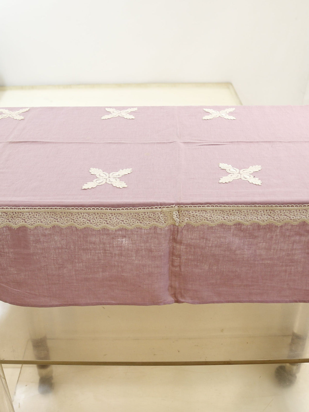 Solid lavender linen table cover with small white embroidered cross motifs and a white crochet lace border
