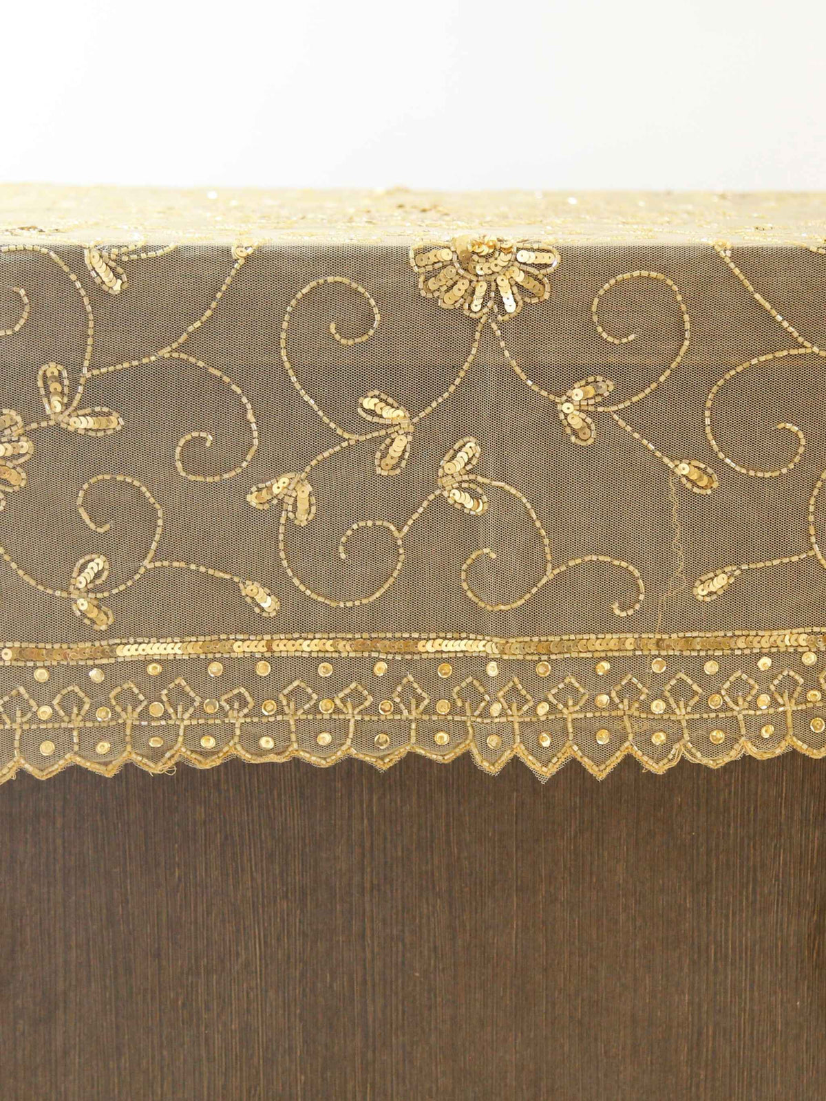 Beige net table cover with a gold sequinned and embroidered floral medallion at the centre and a scalloped lace border