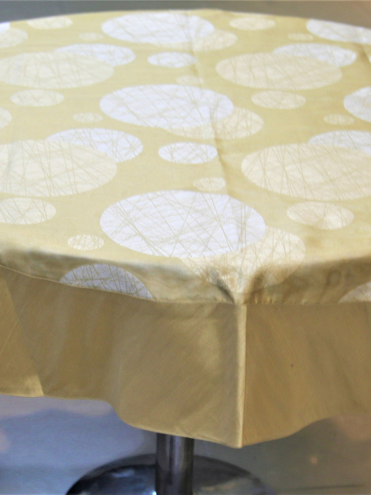 Round pale gold table cover with a white circular thread-art bubble print