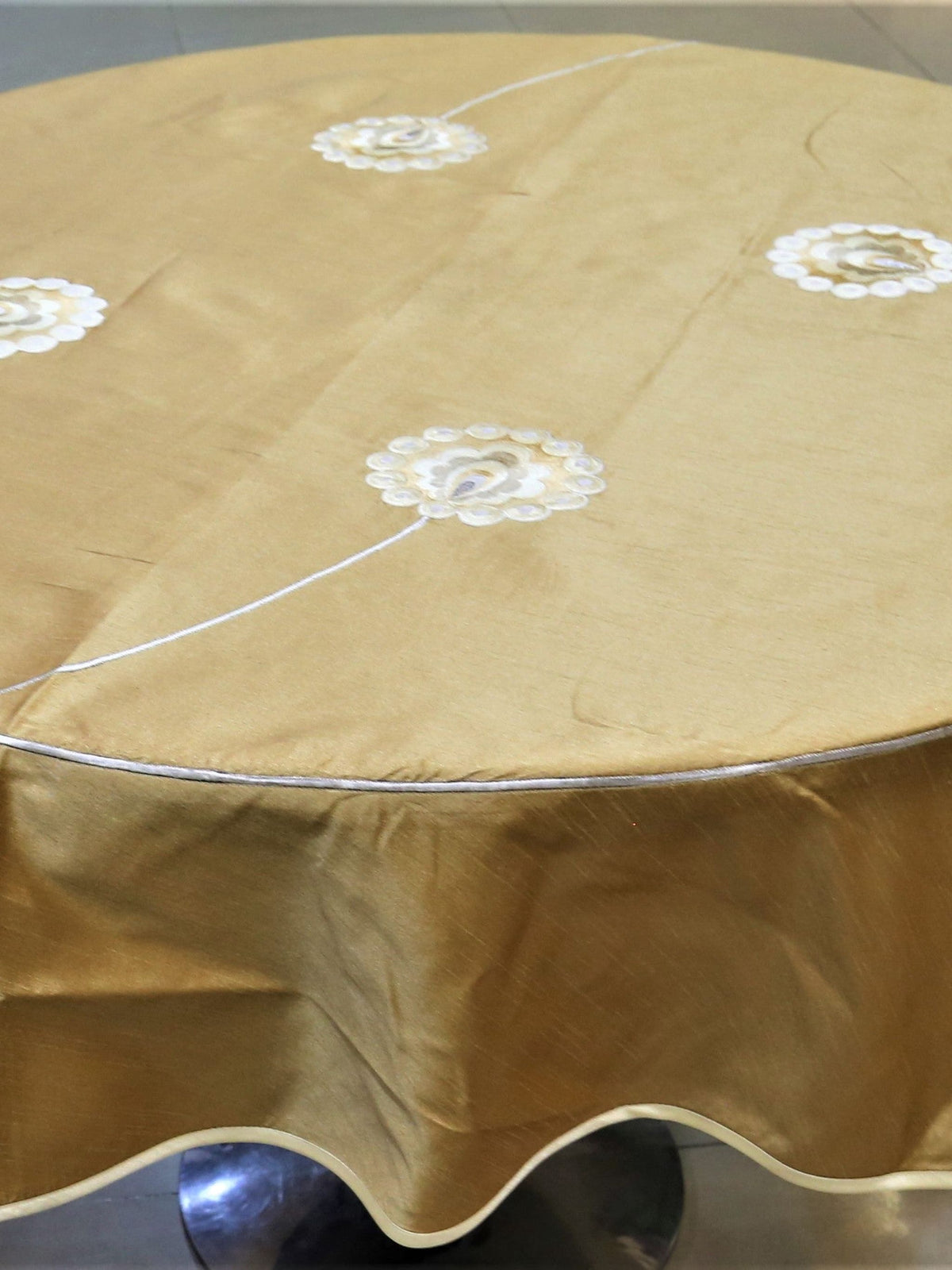Round solid gold table cover with scattered white flower appliqués and a scalloped hem