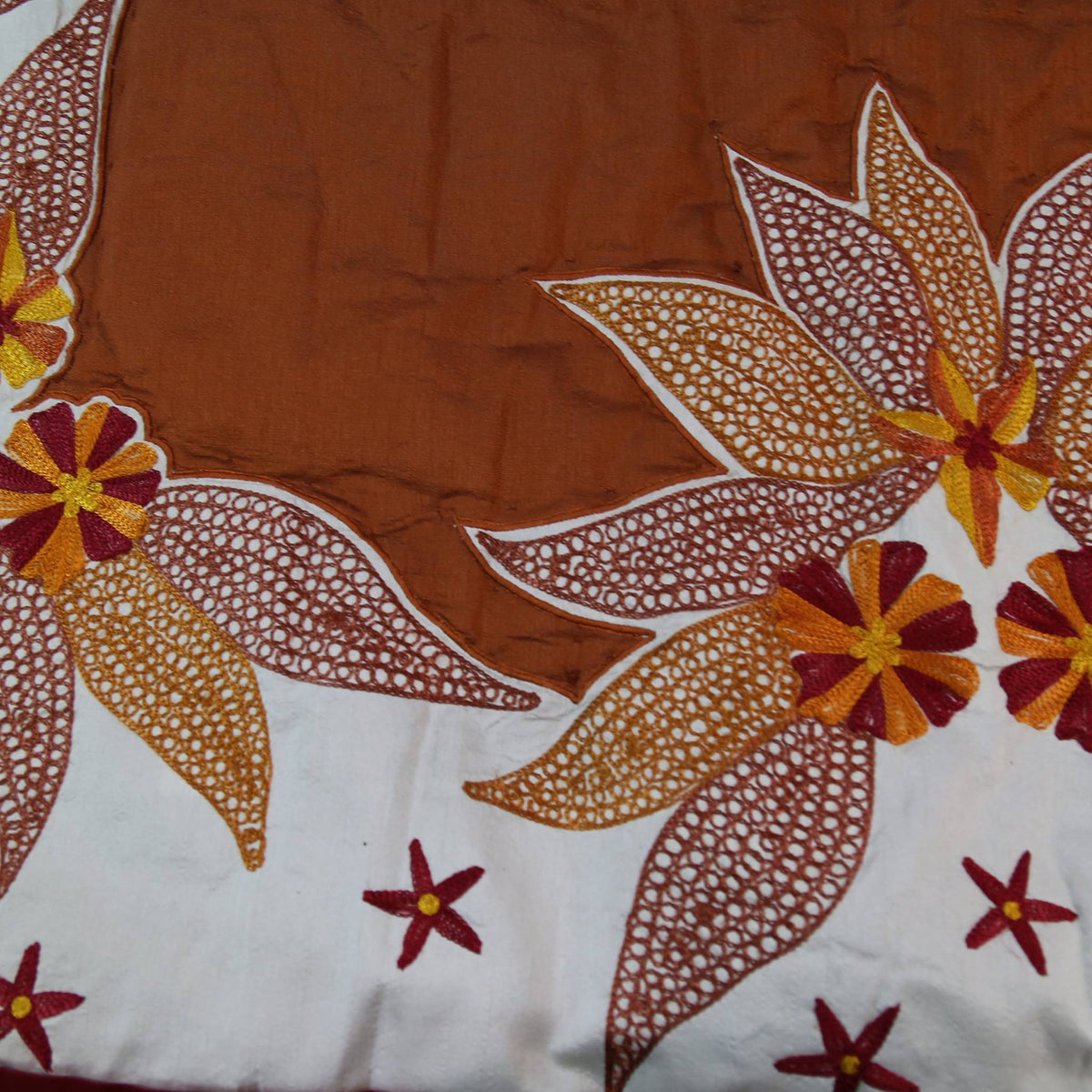 Close up of the rust brown fabric with large cream embroidered lily flowers