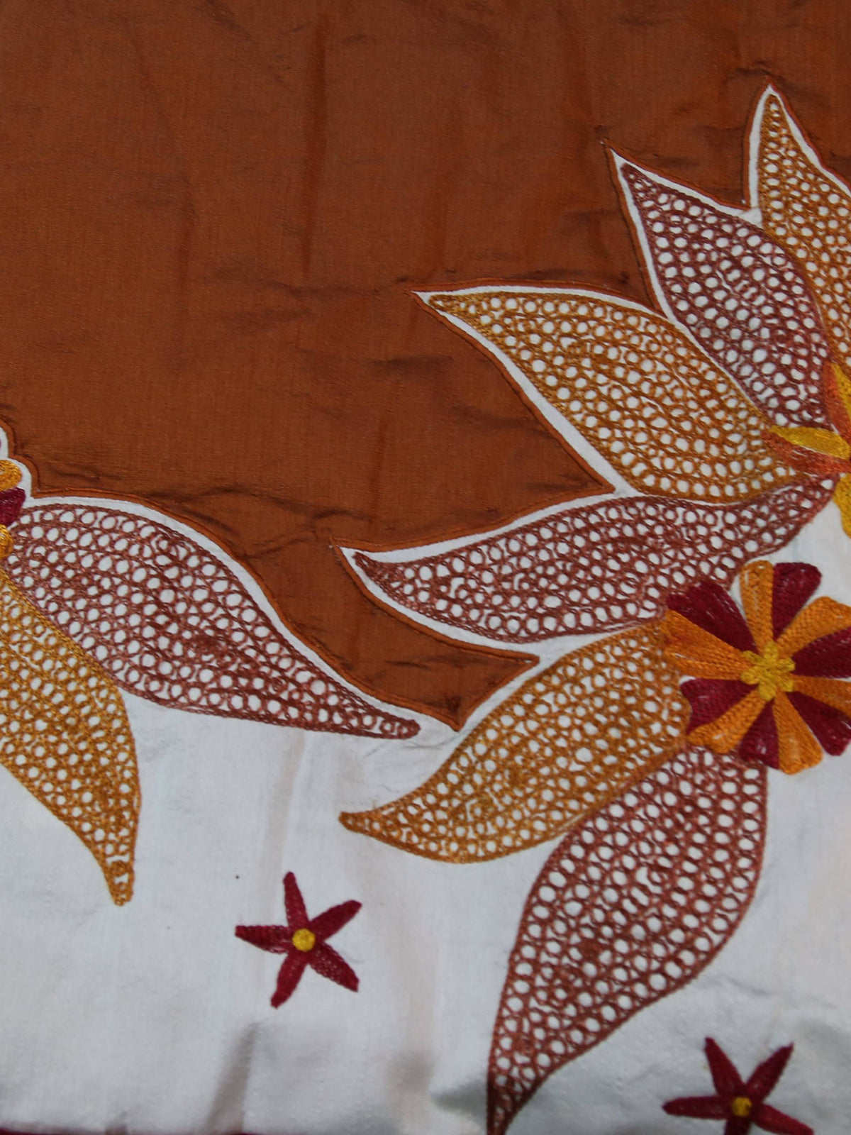 Close up of the rust brown fabric with large cream embroidered lily flowers