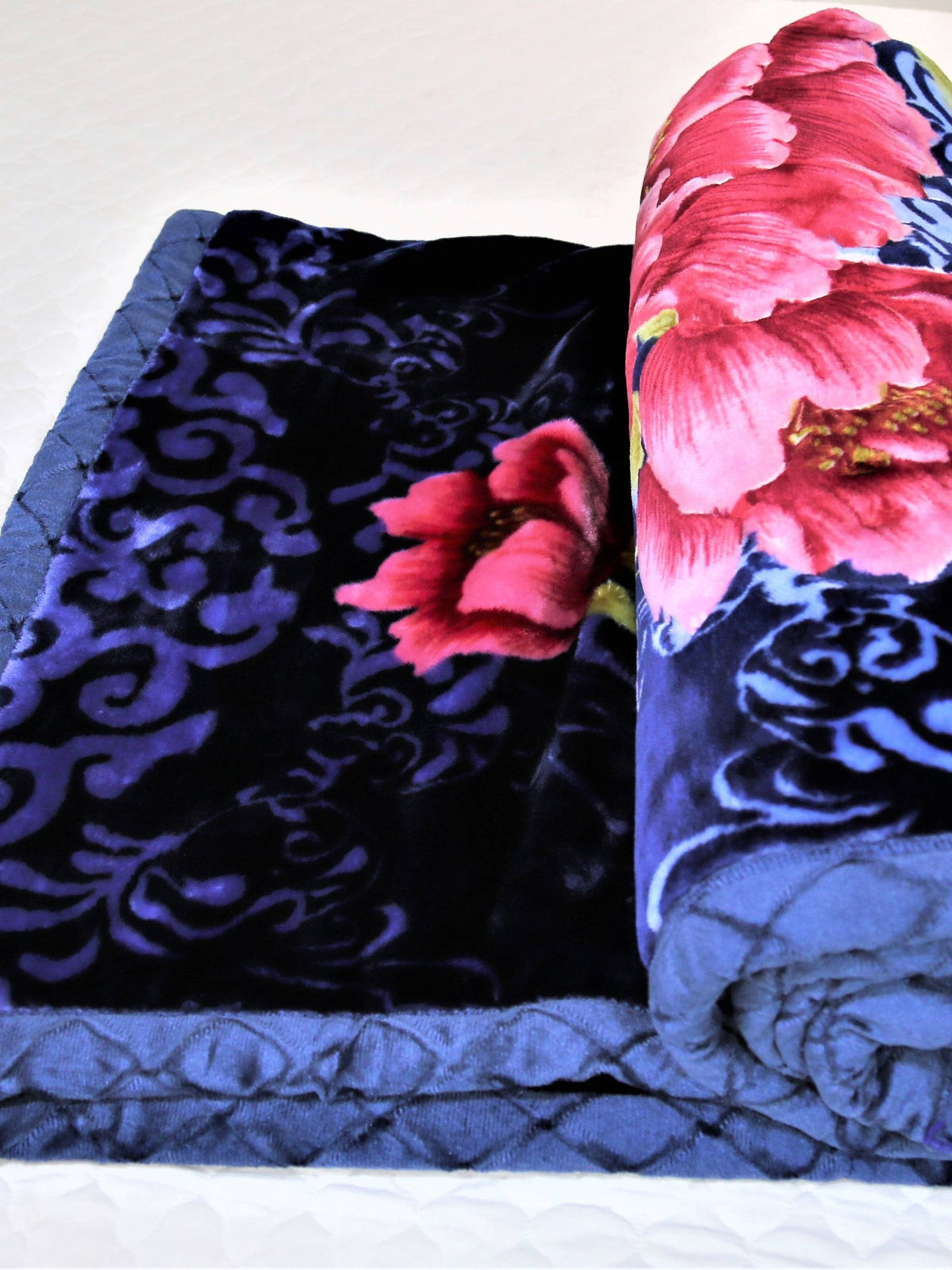 Navy-blue velour blanket rolled up, showing a close-up of the pink peony print and a purple-black scroll section