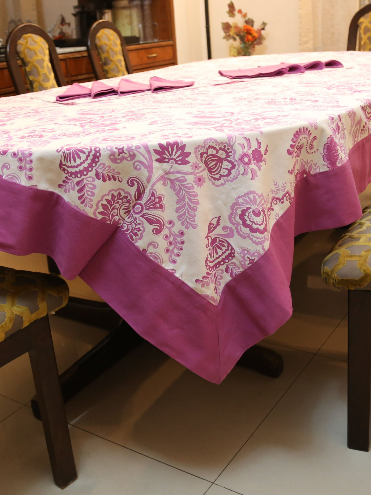 Off-white oval table cover set with a pink and purple paisley floral print, a solid mauve-pink border, and matching mauve triangle-folded napkins