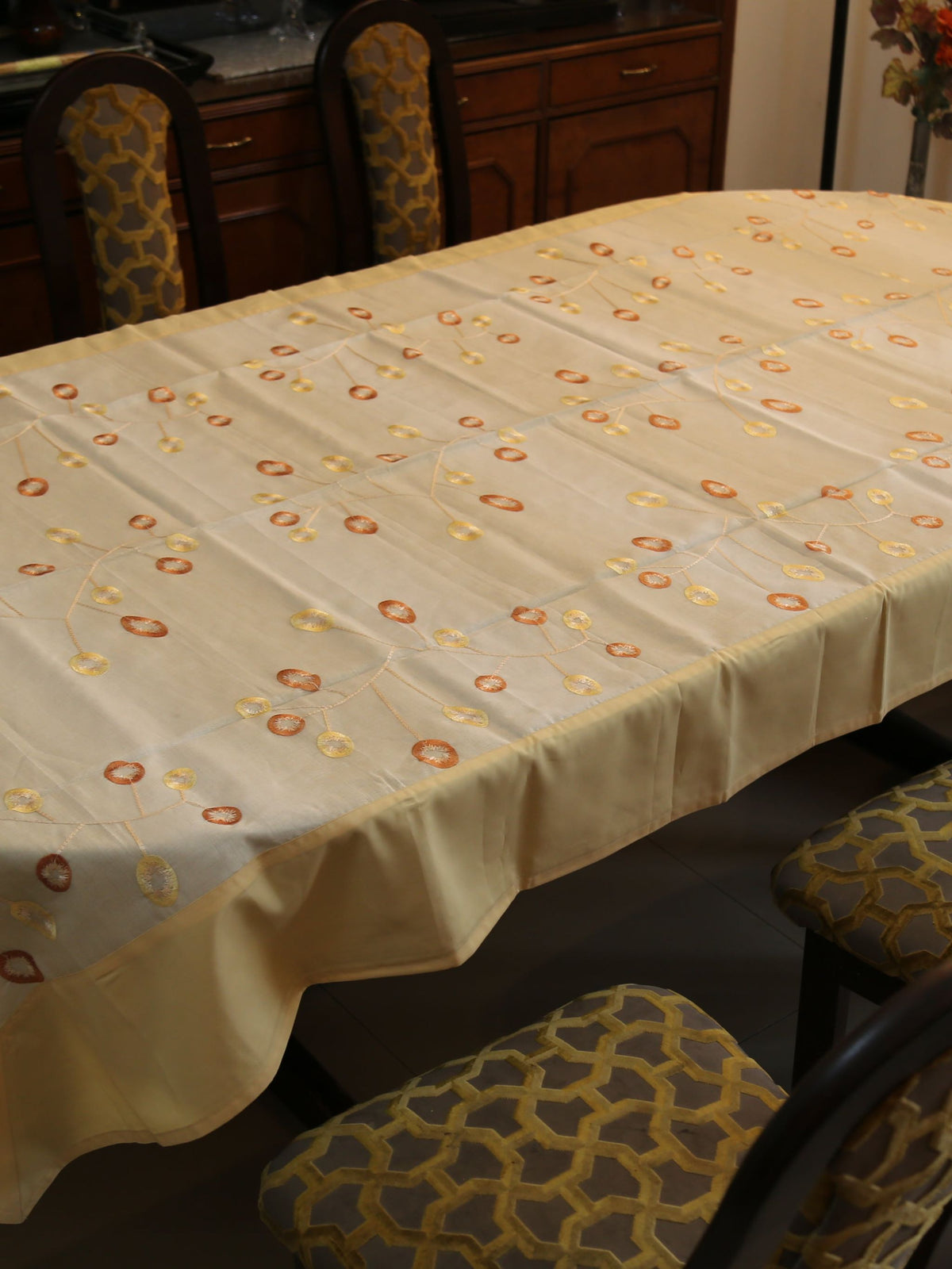 Cream oval table cover with a rust-orange and gold ring embroidery vine pattern and a solid cream border