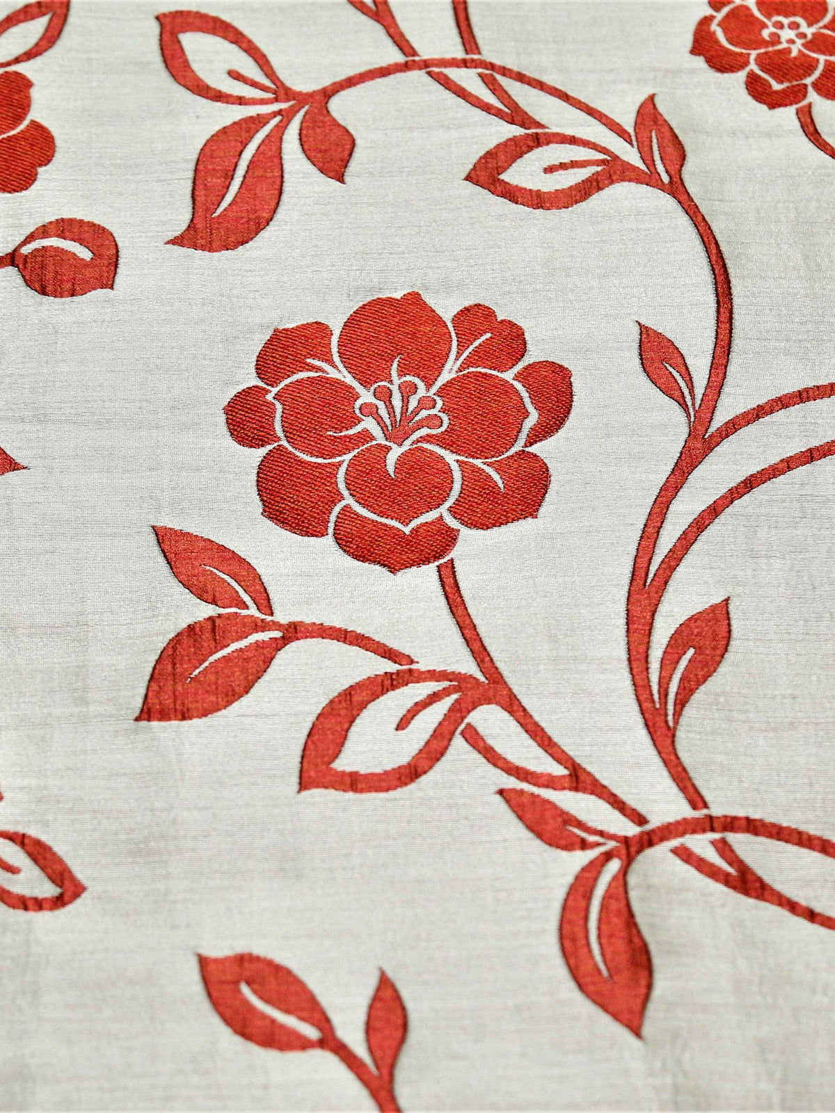 Close up of cream fabric with a red embroidered rose vine on the quilted bedcover